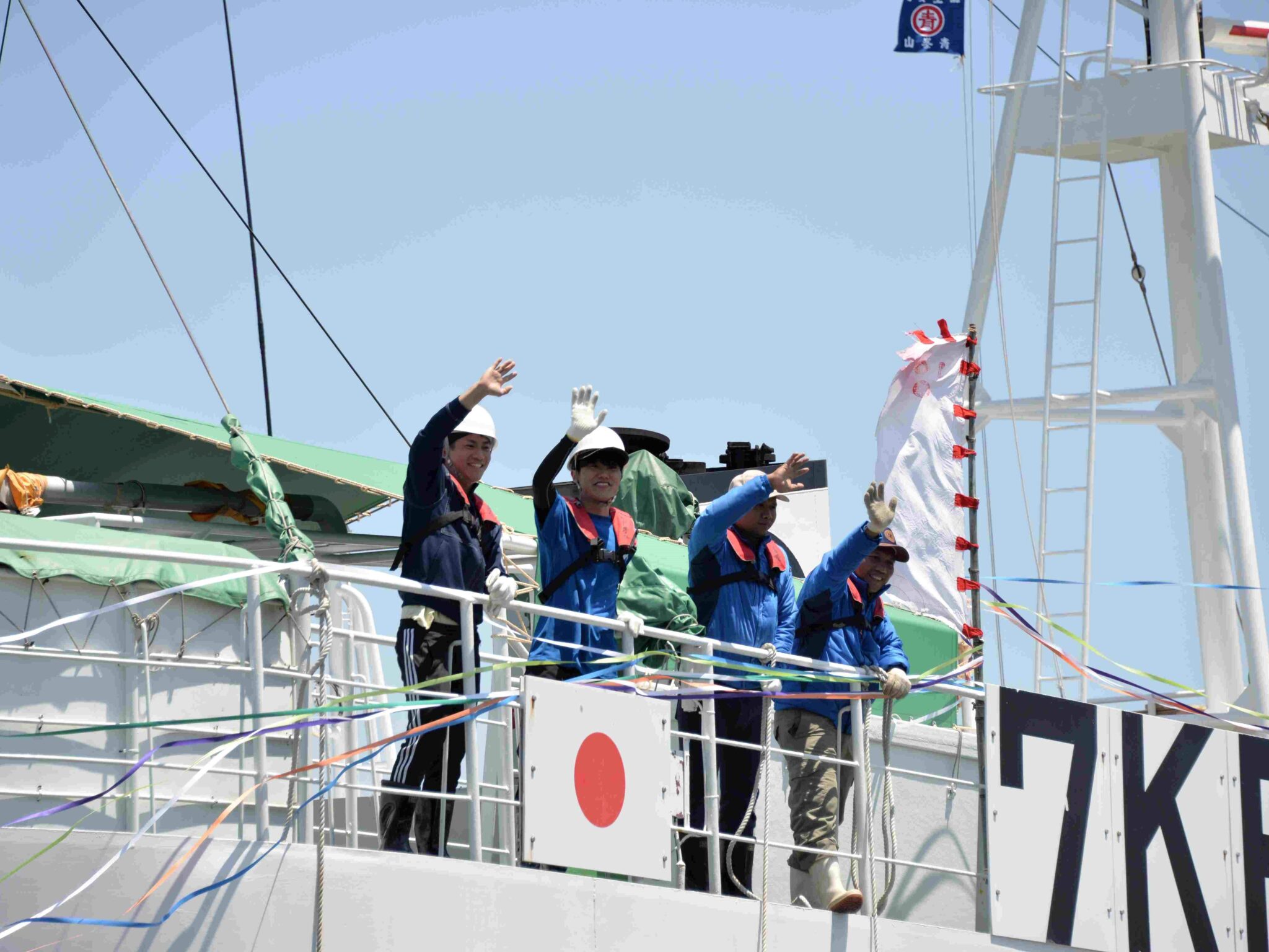船上から笑顔で手を振る若い漁業者たち